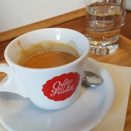 A double espresso in a small white mug with the Coffee & Friends logo