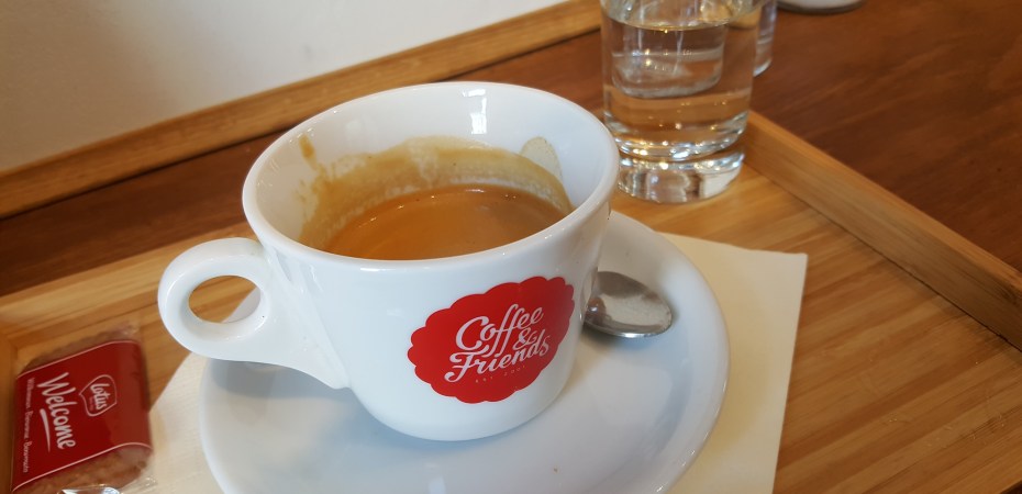 A double espresso in a small white mug with the Coffee & Friends logo